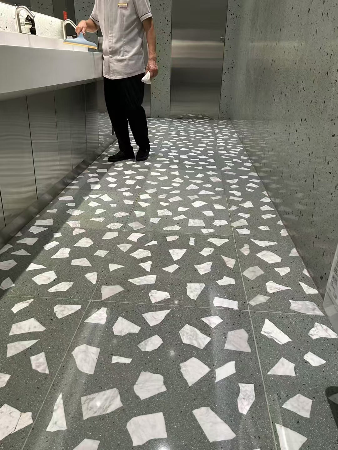 The white marble terrazzo on the floor of the mall's public restroom has a light green background